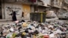 Women walk past piled up garbage after rebels took the main northern city of Aleppo and have since pushed south from their enclave in northwest Syria, Dec. 4, 2024.