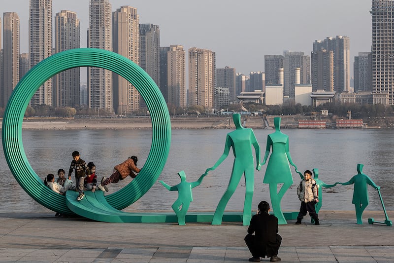 People gather near a statue of a pair of parents that was renovated to add two children in Hankou Park next to Yangtze River in Wuhan, January 5, 2024.