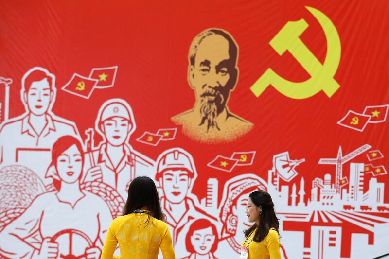 Women wearing traditional long dress \'ao dai\', stand near a giant poster at the National Convention Center, the venue for the upcoming 13th national congress of the ruling Communist Party of Vietnam, in Hanoi, Vietnam January 22, 2021. REUTERS/Kham